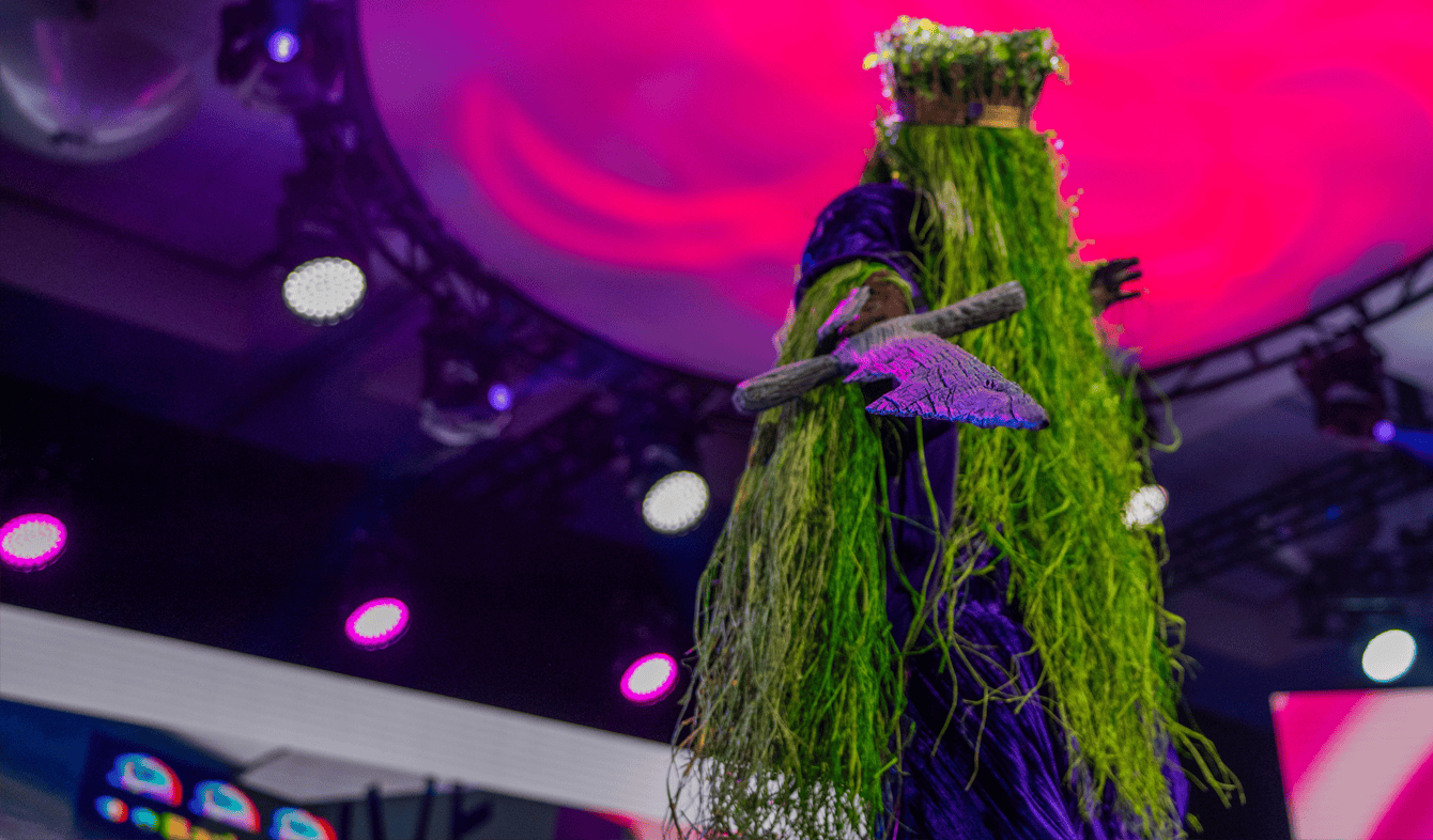 Costumed performer on stage under pink lights